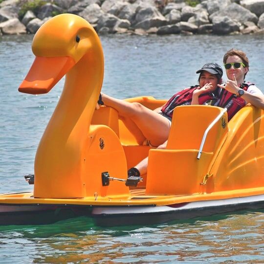 A young man and girl riding on a swan shaped paddleboat on a lake